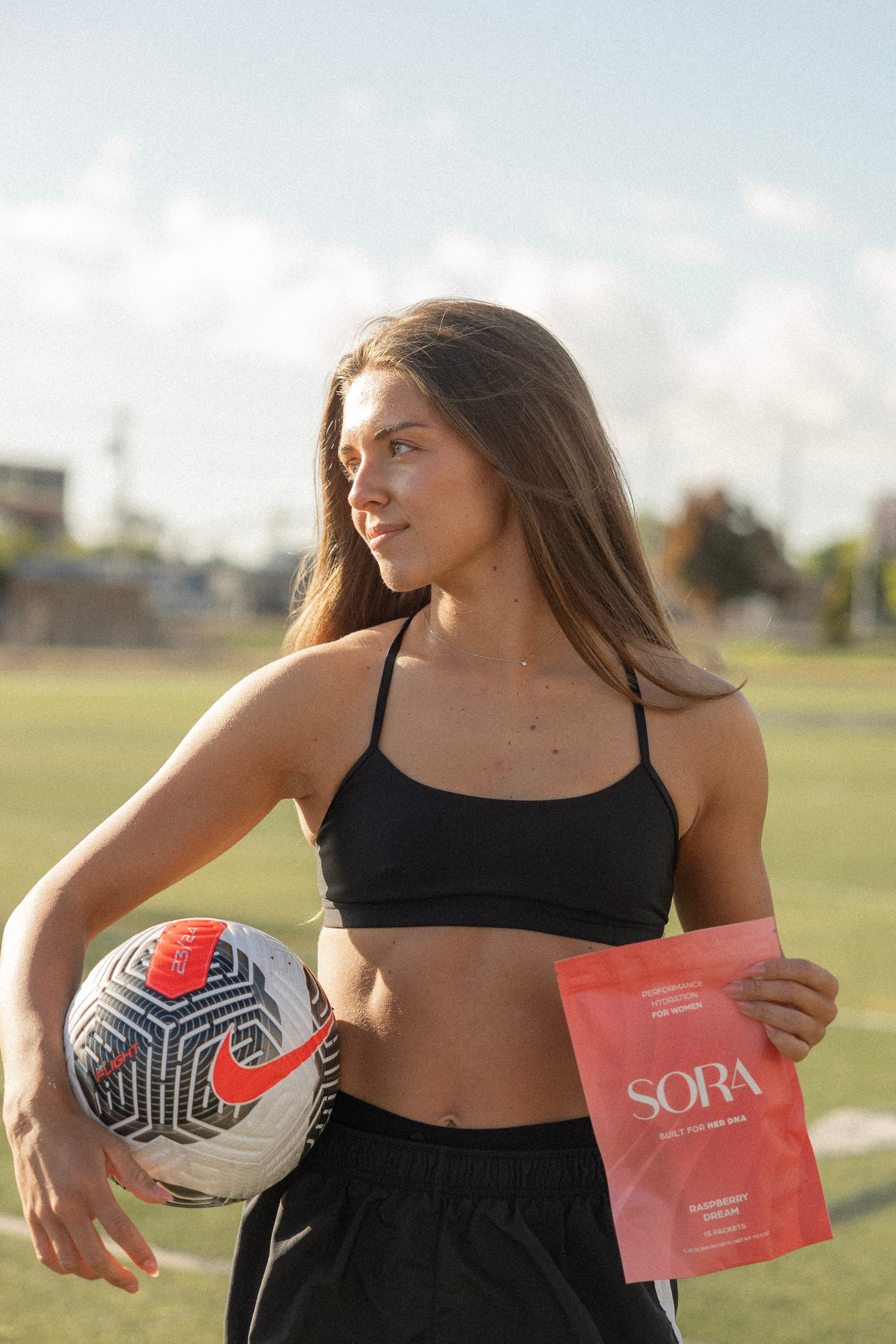 Woman holding a soccer ball and a red book titled 'Sora' on a sports field.