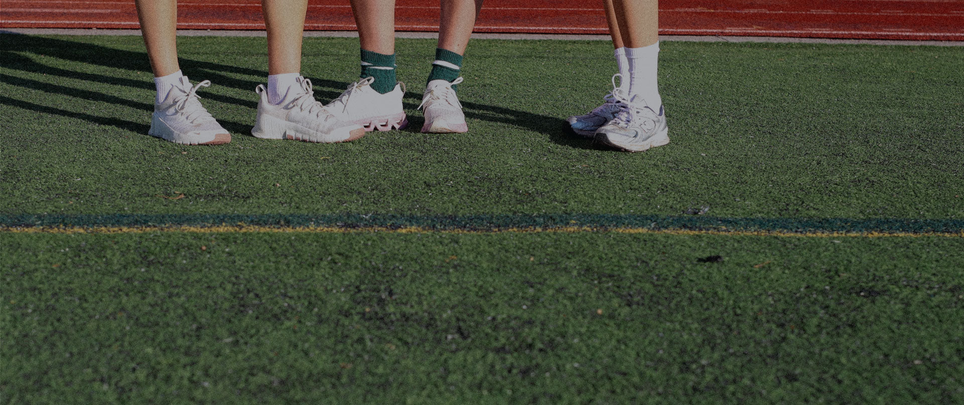 Two pairs of legs wearing white sneakers on a grassy field.